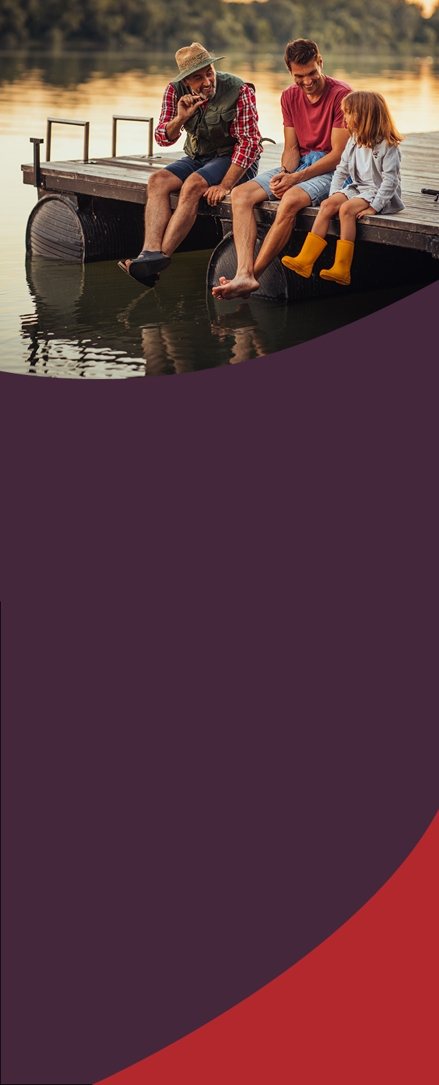 Man laughing with his son and granddaughter sitting on a dock